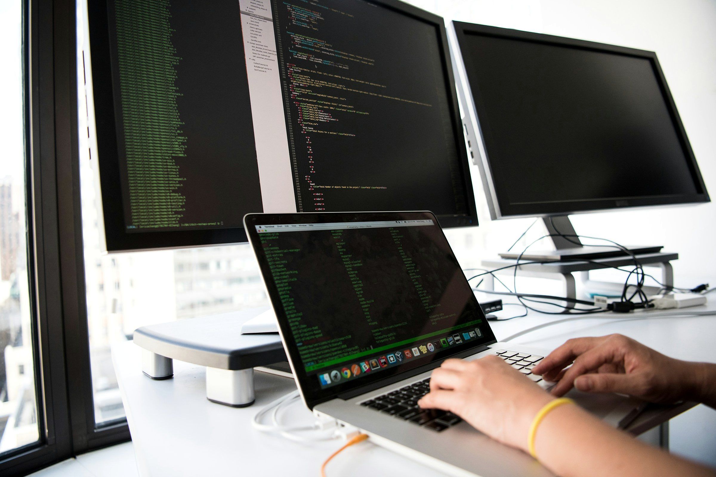 Hände am Laptop vor Bildschirmen mit Quellcode