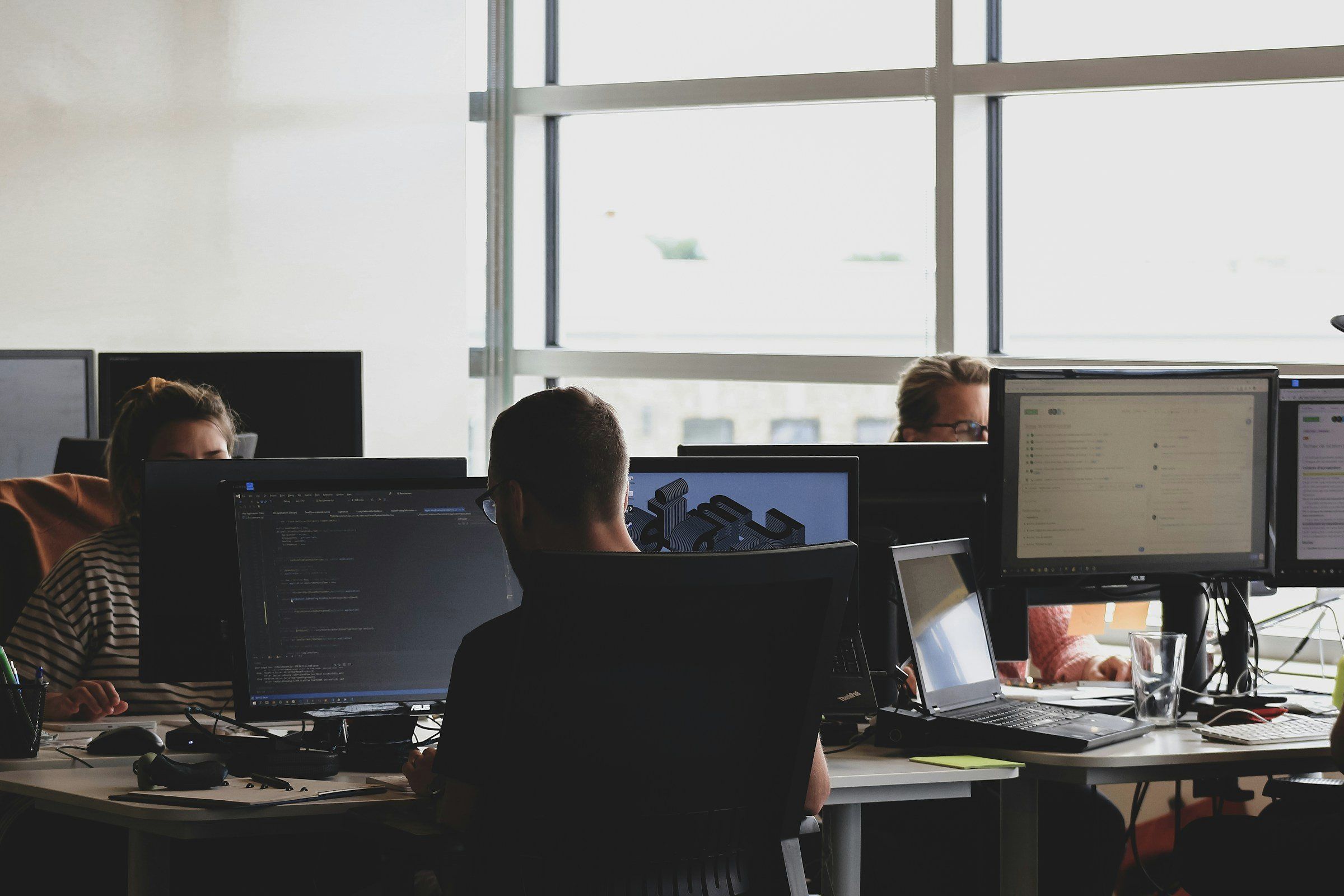 Team arbeitet an Bildschirmen in einem hellen Büro, Ansicht von hinten